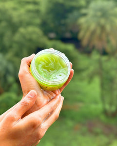 Hand holding shampoo butter against a blurred natural background